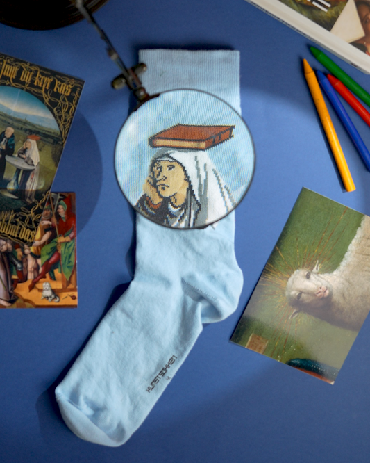 A light blue crew sock with a circular printed illustration of a woman under a magnifying glass and a book floating above her head, styled in a flat-lay on a blue background with vintage magazines, colored pencils, and cards.